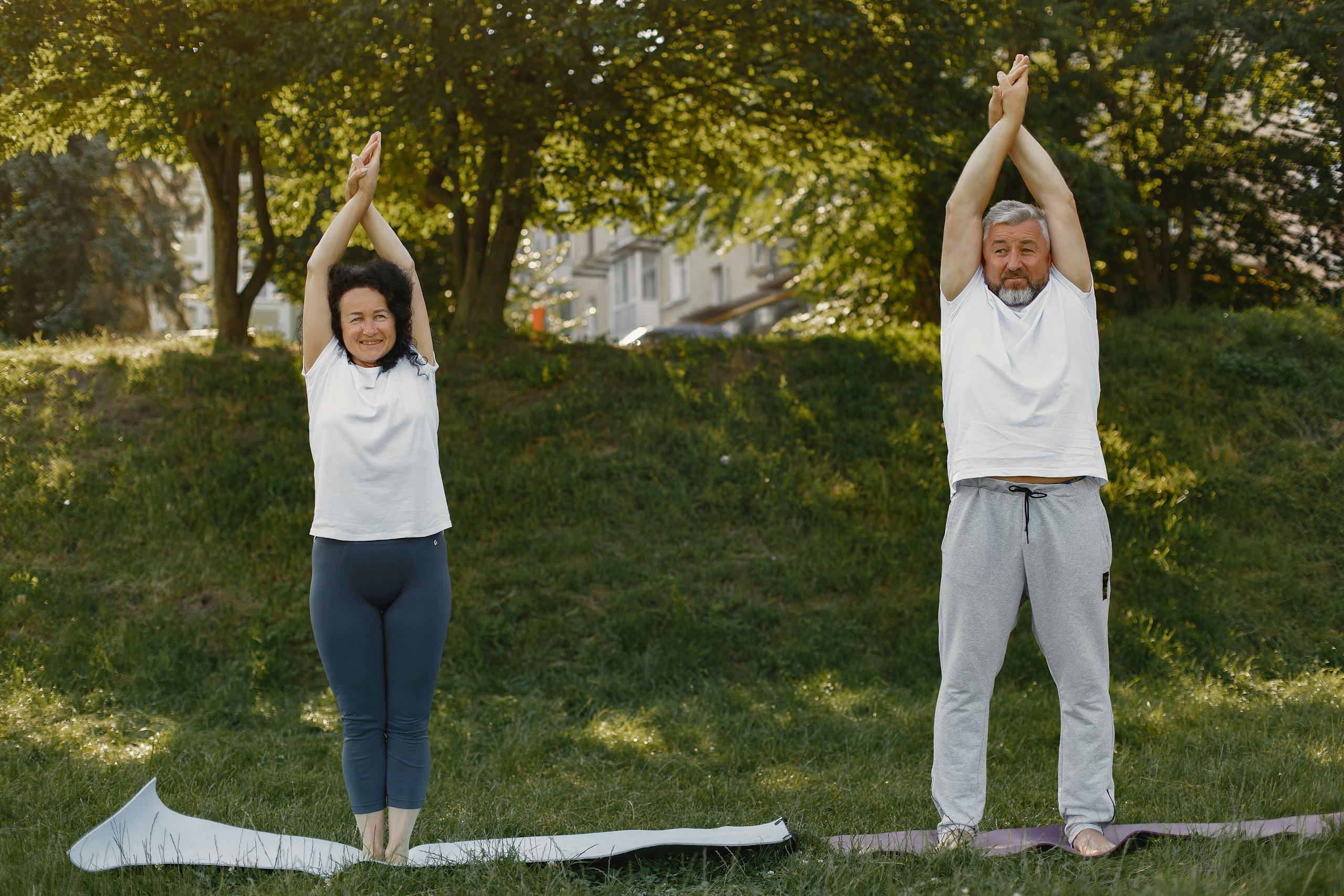 A senior couple in activewear practicing yoga in a sunny park, promoting fitness and healthy living.